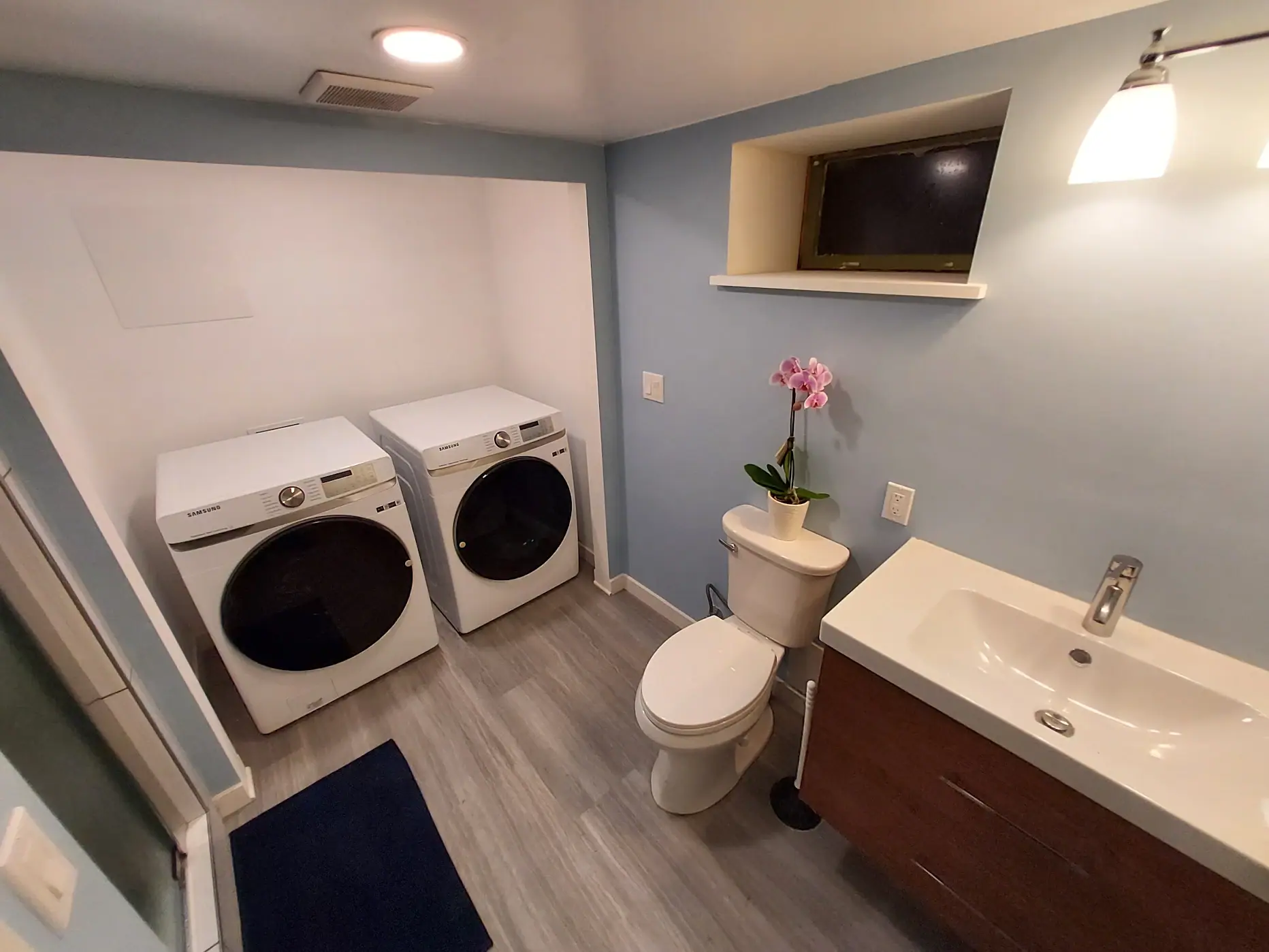 Bathroom with a wall-hung vanity, toilet and wood-look flooring next to a laundry area