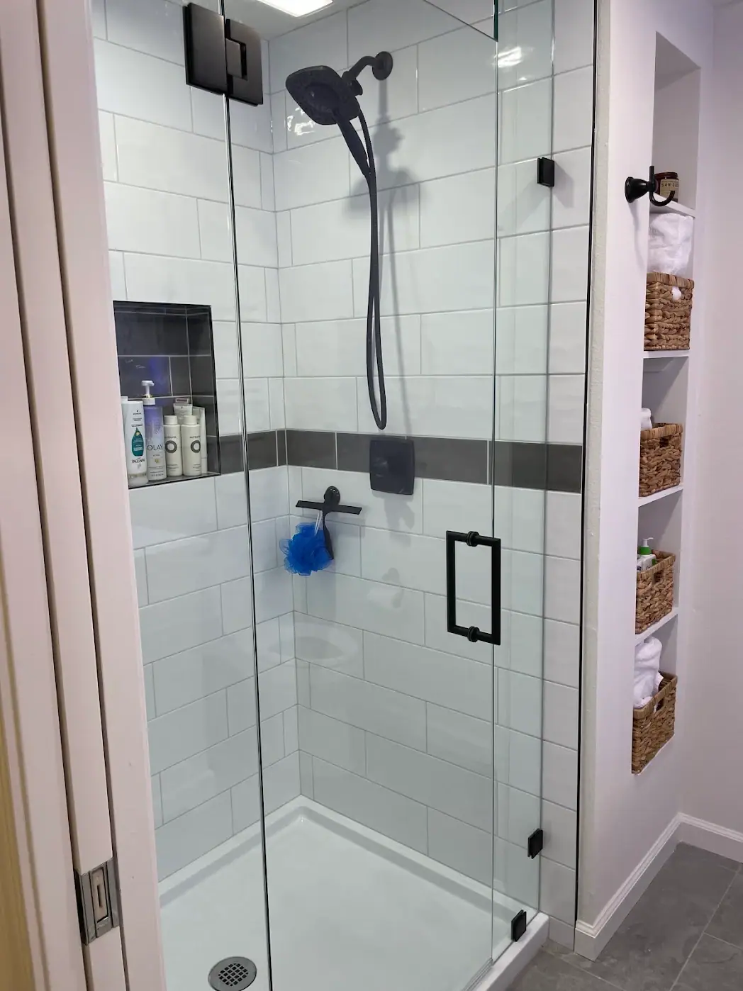 Shower with large white tile, a dark accent band, a tiled niche, a frameless glass enclosure and matte black fixtures