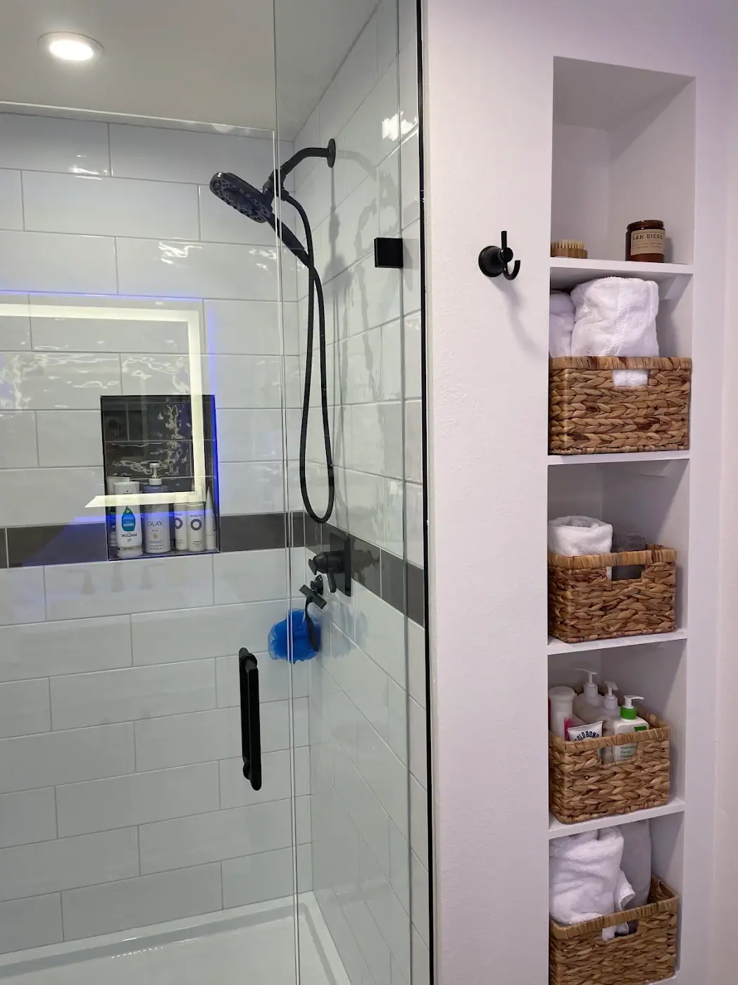 Glass shower beside built-in open shelving with storage baskets