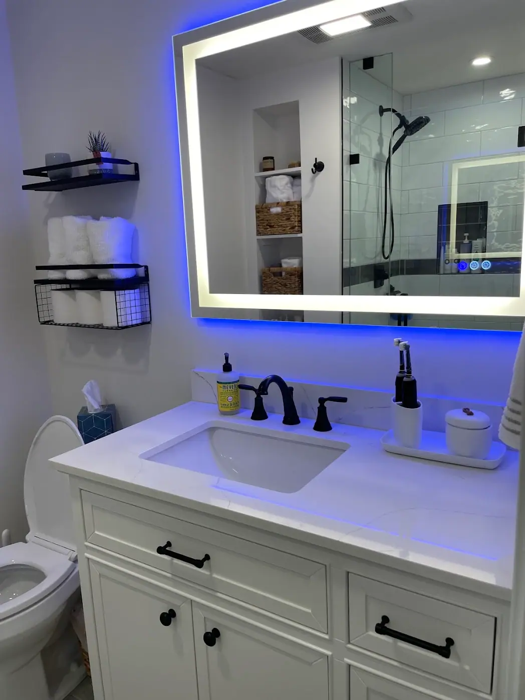 White vanity with a veined countertop, matte black faucet and hardware and a lighted mirror