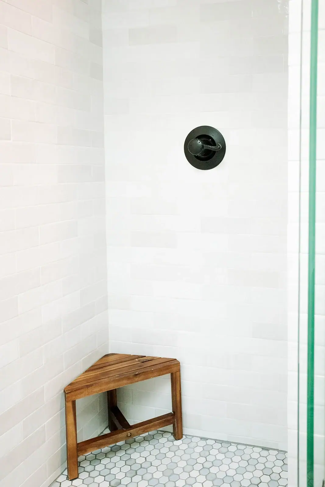 Walk-in shower with white tile walls, hexagon mosaic floor, corner bench and matte black controls