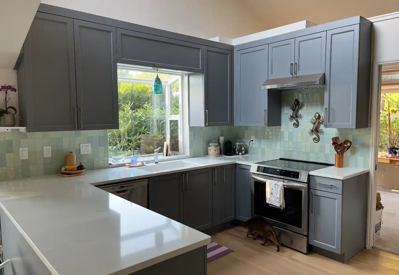 U-shaped kitchen with gray shaker cabinets, white countertops, a green glazed tile backsplash and a window over the sink