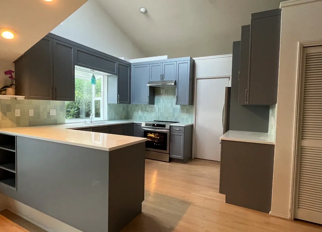 Gray kitchen under a vaulted ceiling with a peninsula, white countertops and light wood flooring