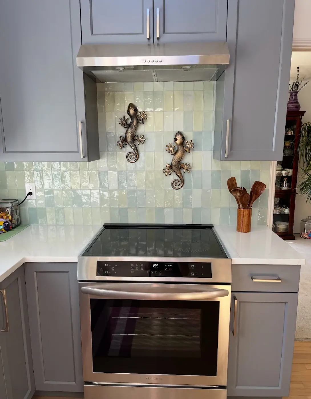 Range wall with gray cabinets, a stainless range hood and a green glazed tile backsplash
