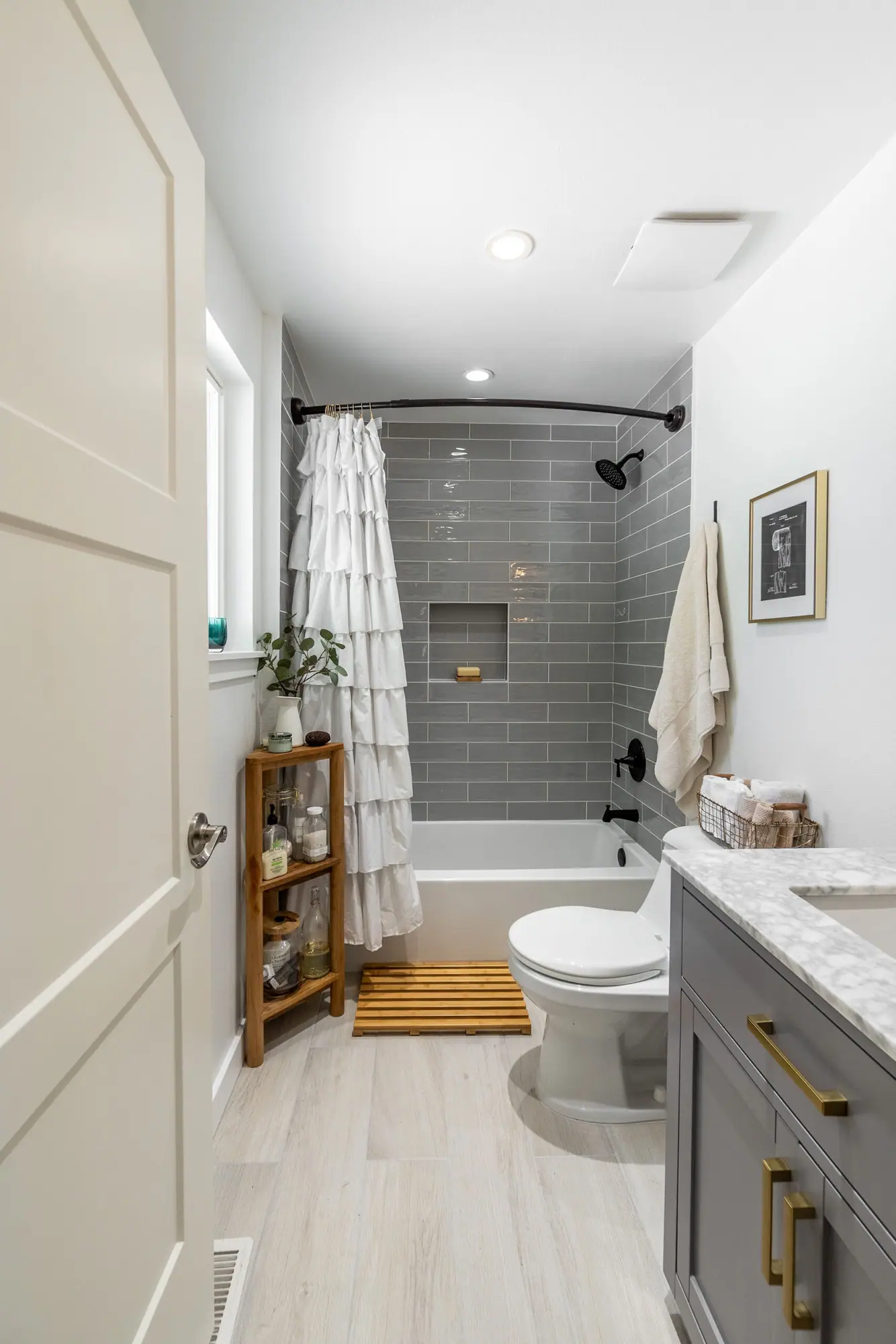 Bathroom with a gray subway tile tub surround, built-in niche, gray vanity and wood-look floor tile