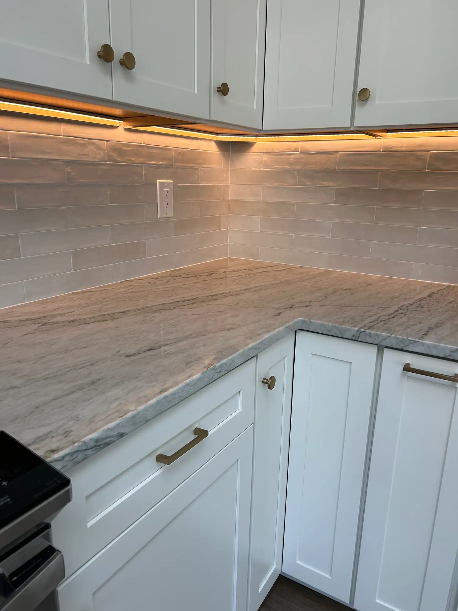 Corner countertop with a veined surface, glossy tile backsplash and under-cabinet lighting