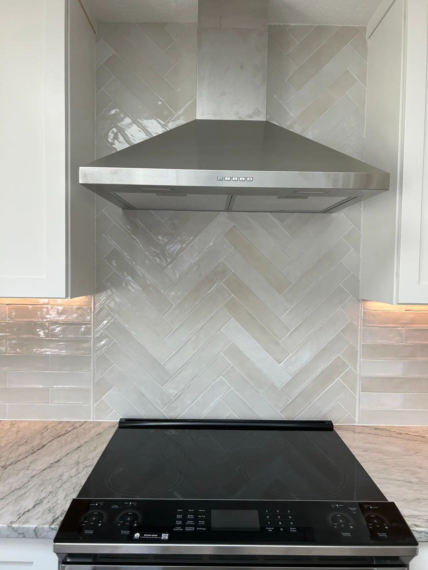 Herringbone tile backsplash behind the range with a stainless hood and under-cabinet lighting