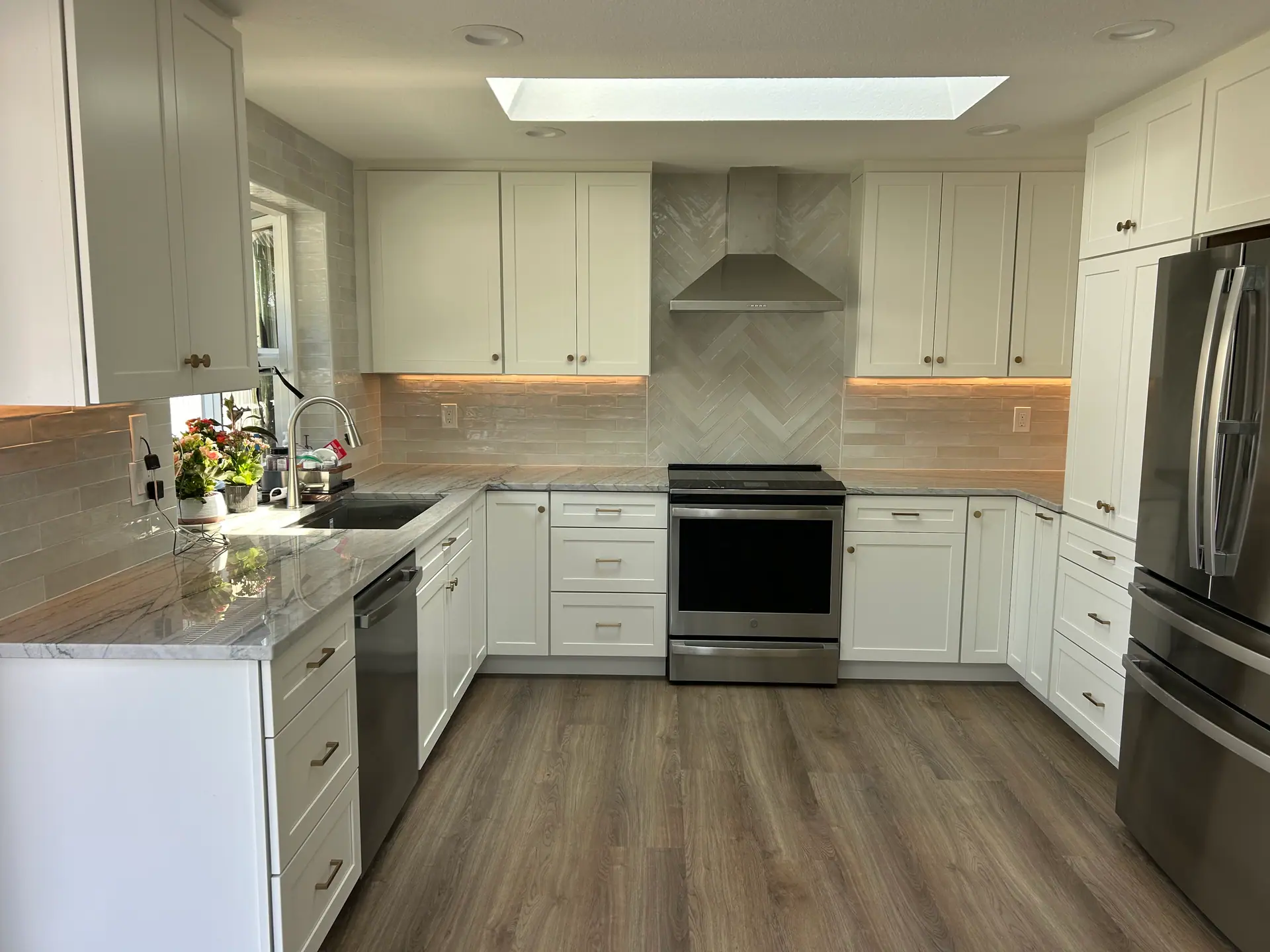 White shaker kitchen with herringbone tile at the range, veined countertops, stainless appliances and wood-look flooring
