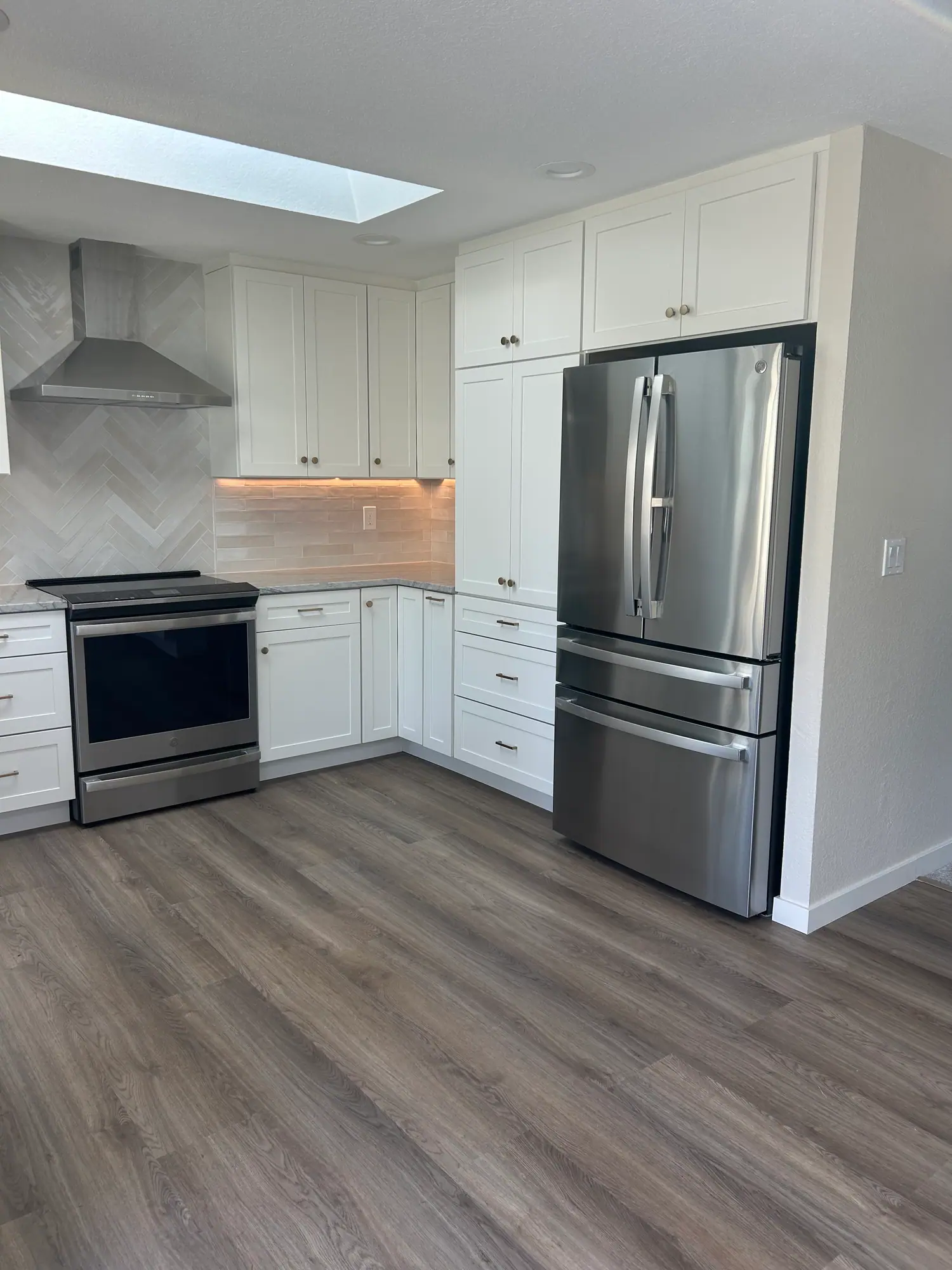 White kitchen under a skylight with a stainless refrigerator and range and wood-look flooring