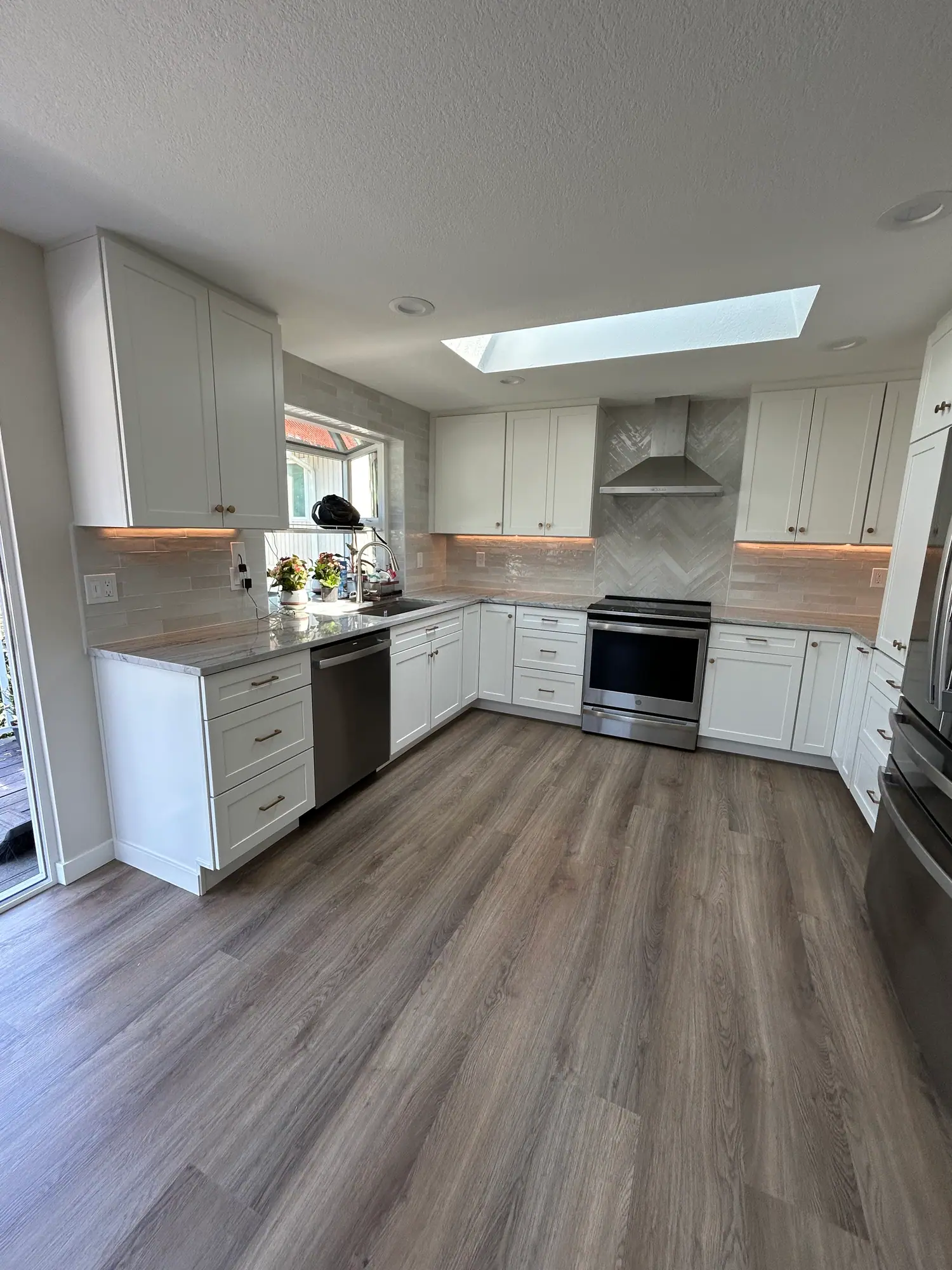 U-shaped white kitchen with a skylight and wood-look flooring