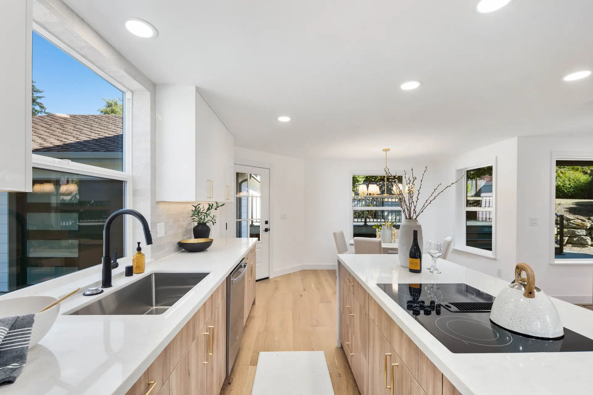 Long kitchen island with a cooktop across from an undermount sink and light wood cabinetry