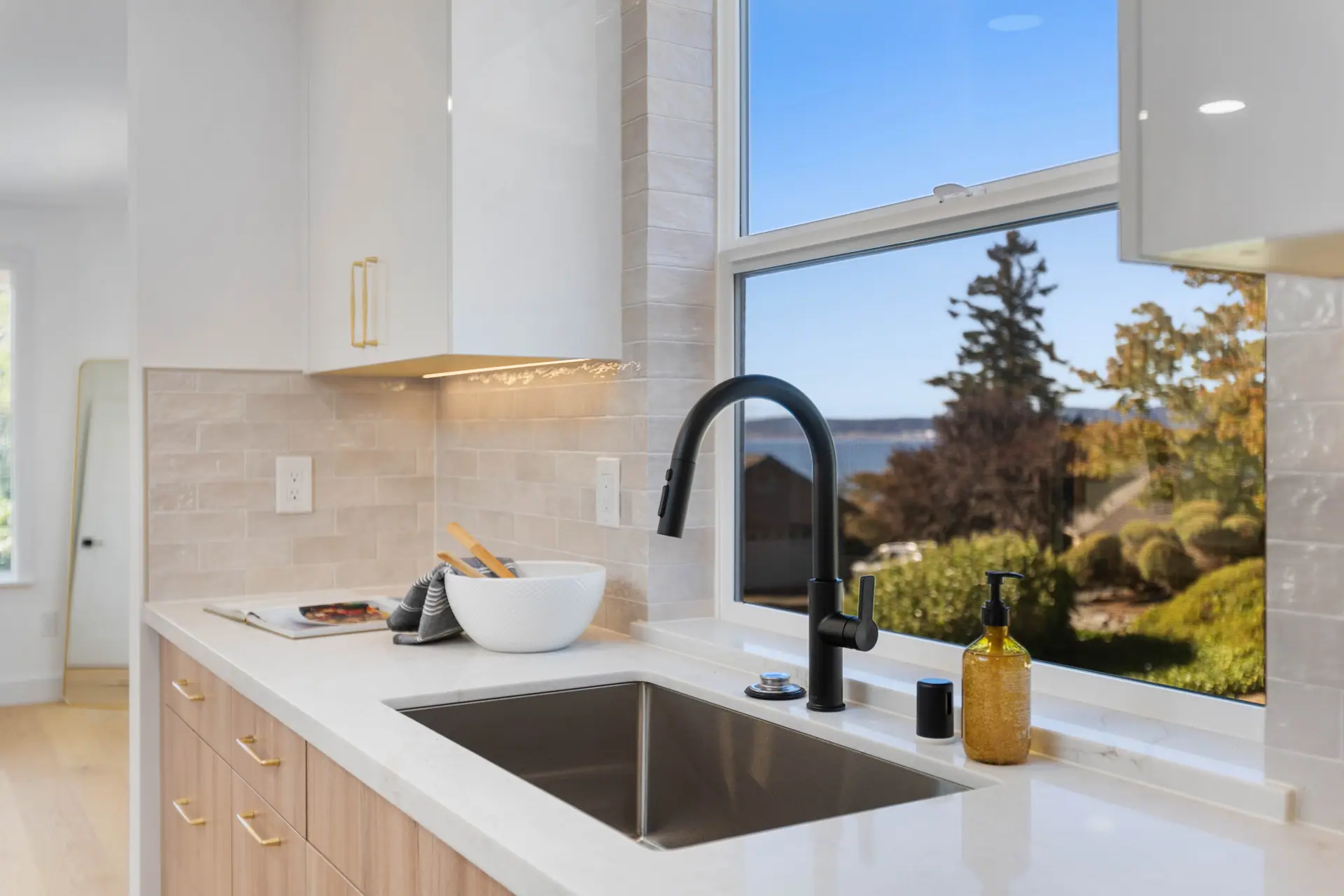 Undermount sink with a matte black faucet, tile backsplash and under-cabinet lighting beside a large window