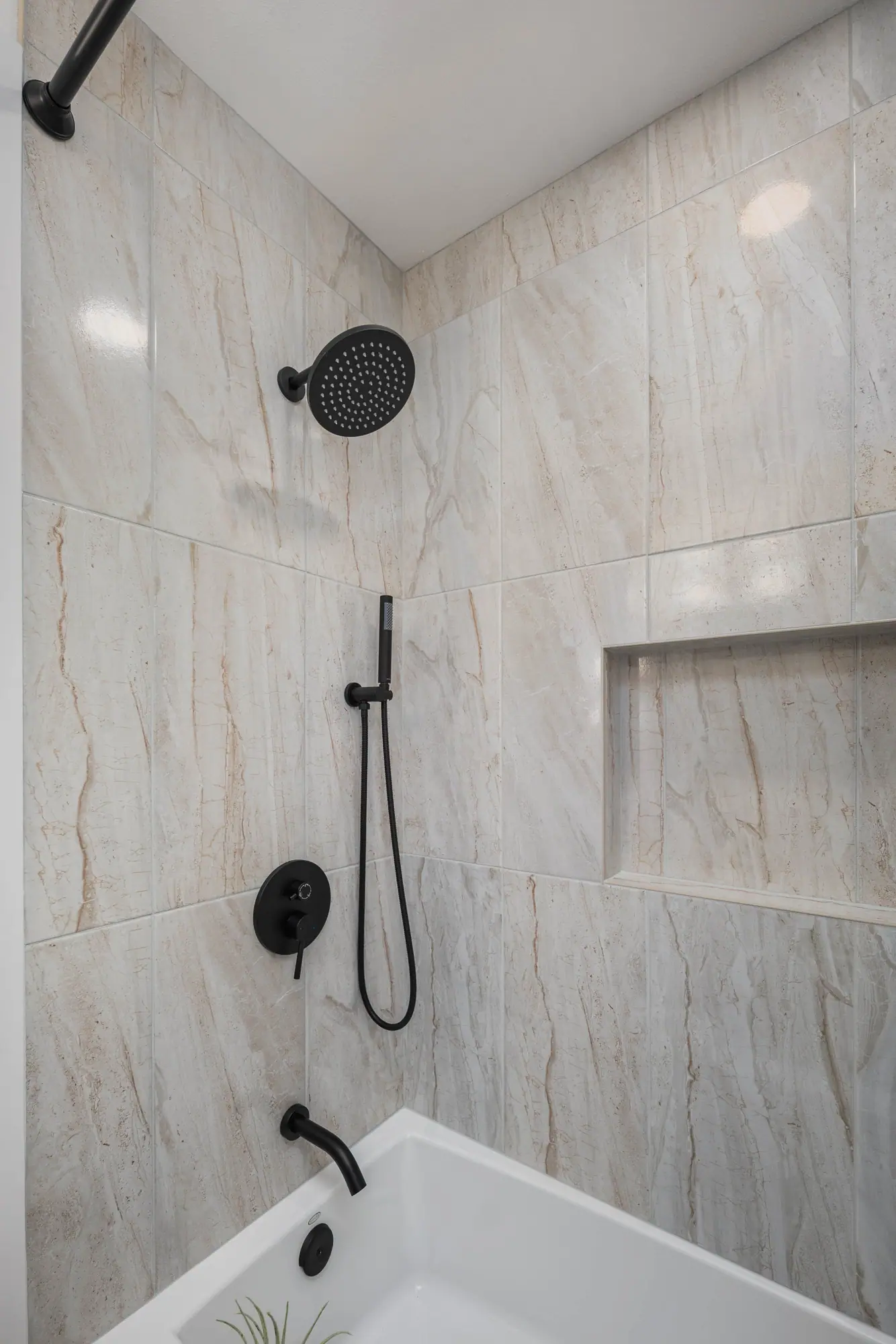 Tub and shower with large-format stone-look tile, a built-in niche and matte black fixtures