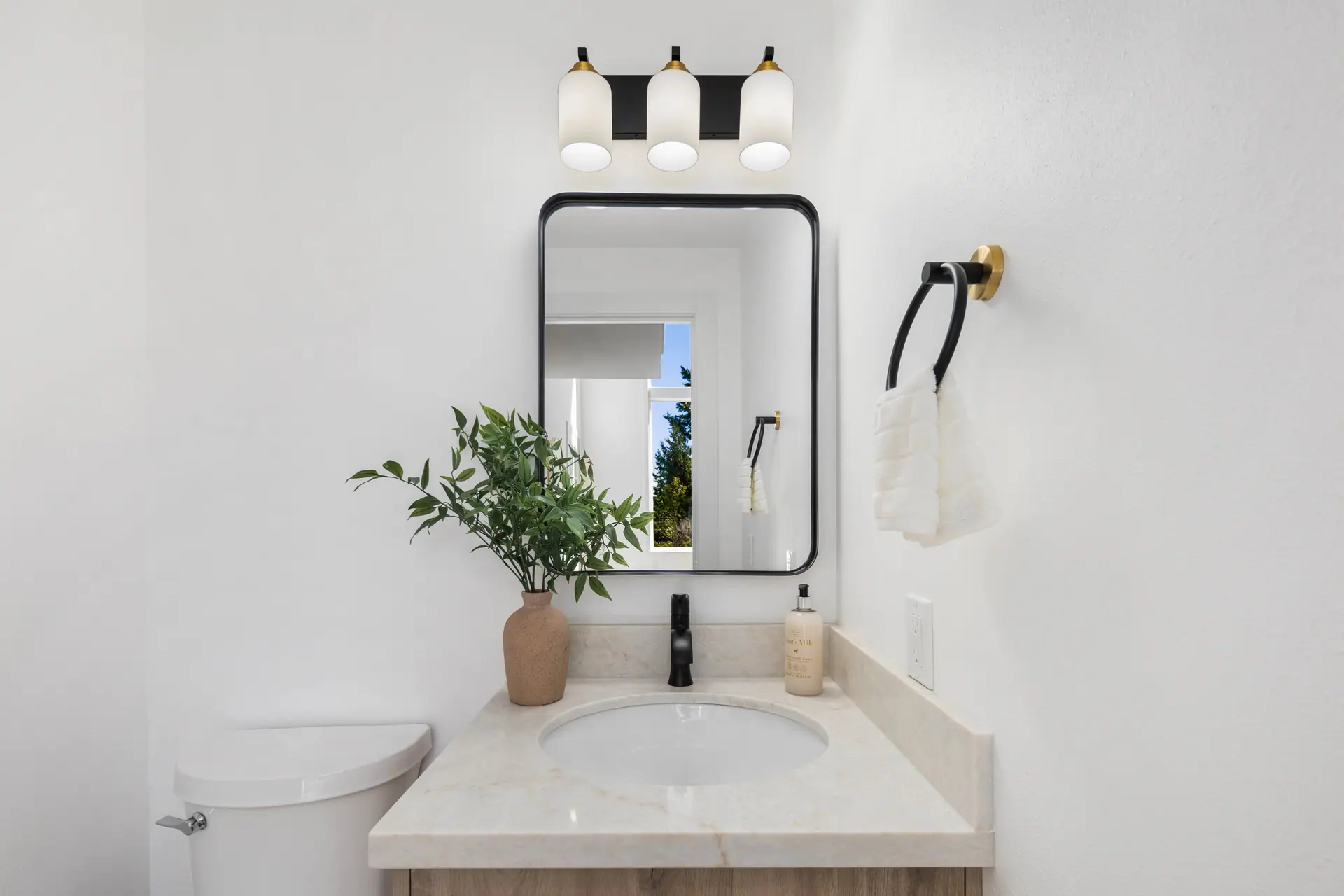 Bathroom vanity with a light wood cabinet, black-framed mirror and three-light fixture