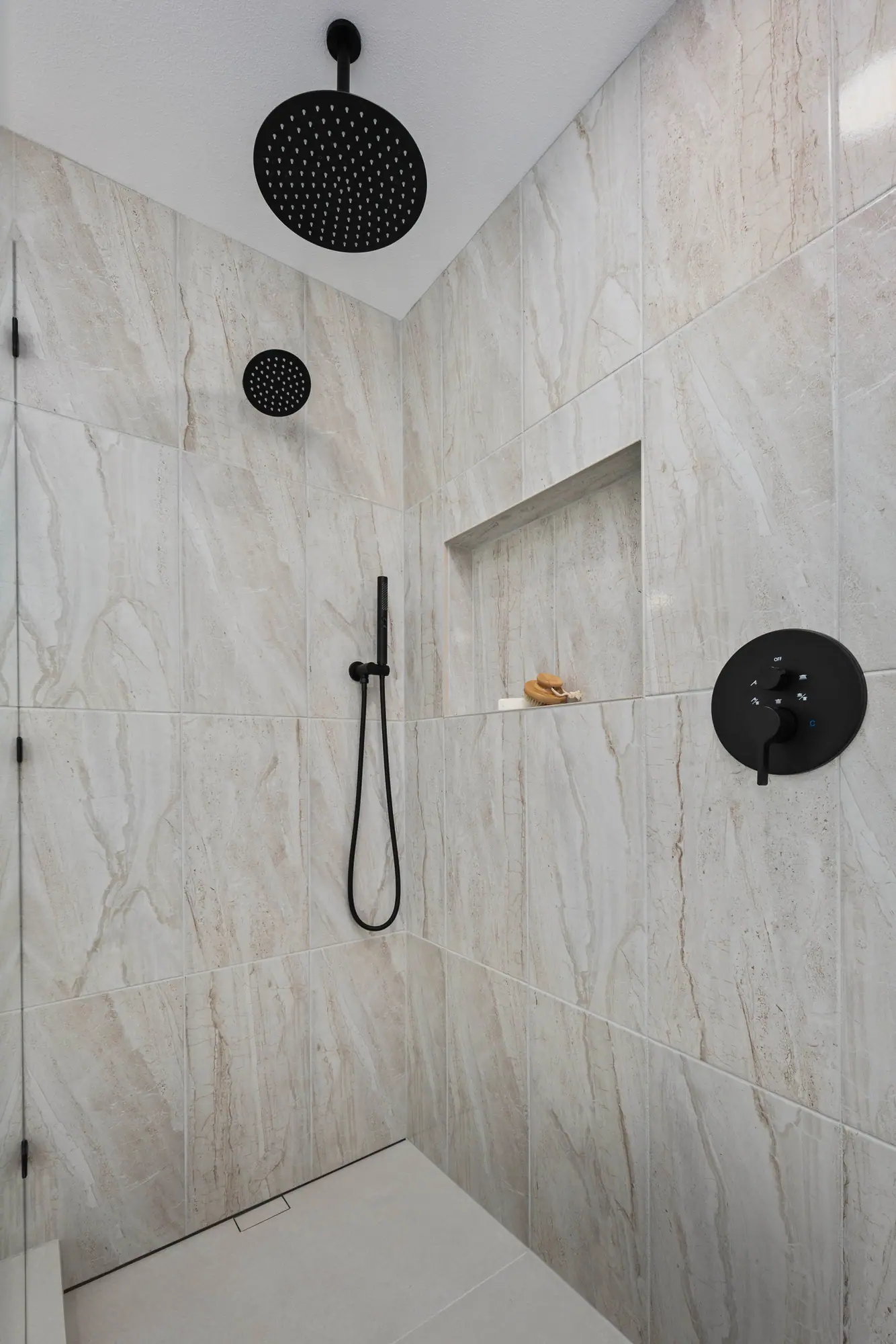 Walk-in shower with large-format stone-look tile, a built-in niche and a matte black rain shower