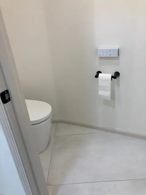 Toilet room with large-format floor tile and a matte black paper holder