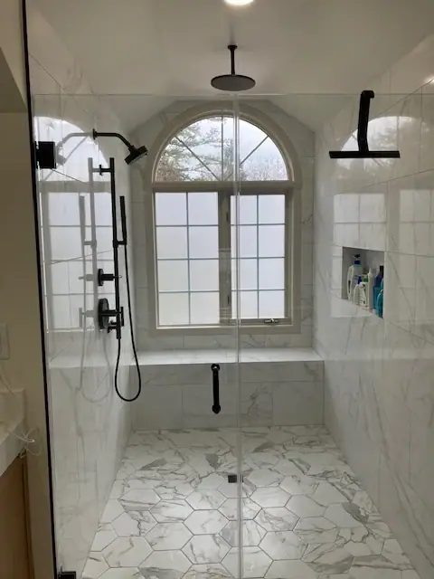 Walk-in shower with marble-look tile, a hexagon mosaic floor, a bench below an arched window and matte black fixtures
