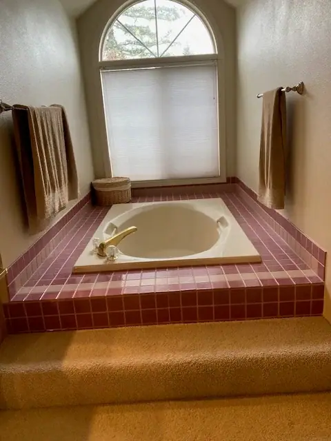 Before the remodel: a pink-tiled drop-in tub under an arched window