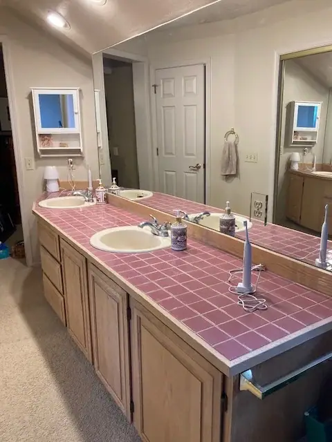 Before the remodel: a long vanity with a pink tile countertop and carpet on the floor