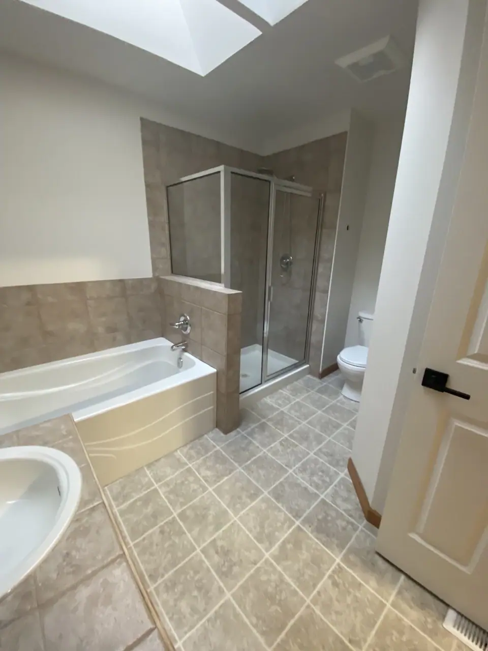Before the remodel: a built-in tub with tile surround and a framed corner shower under a skylight