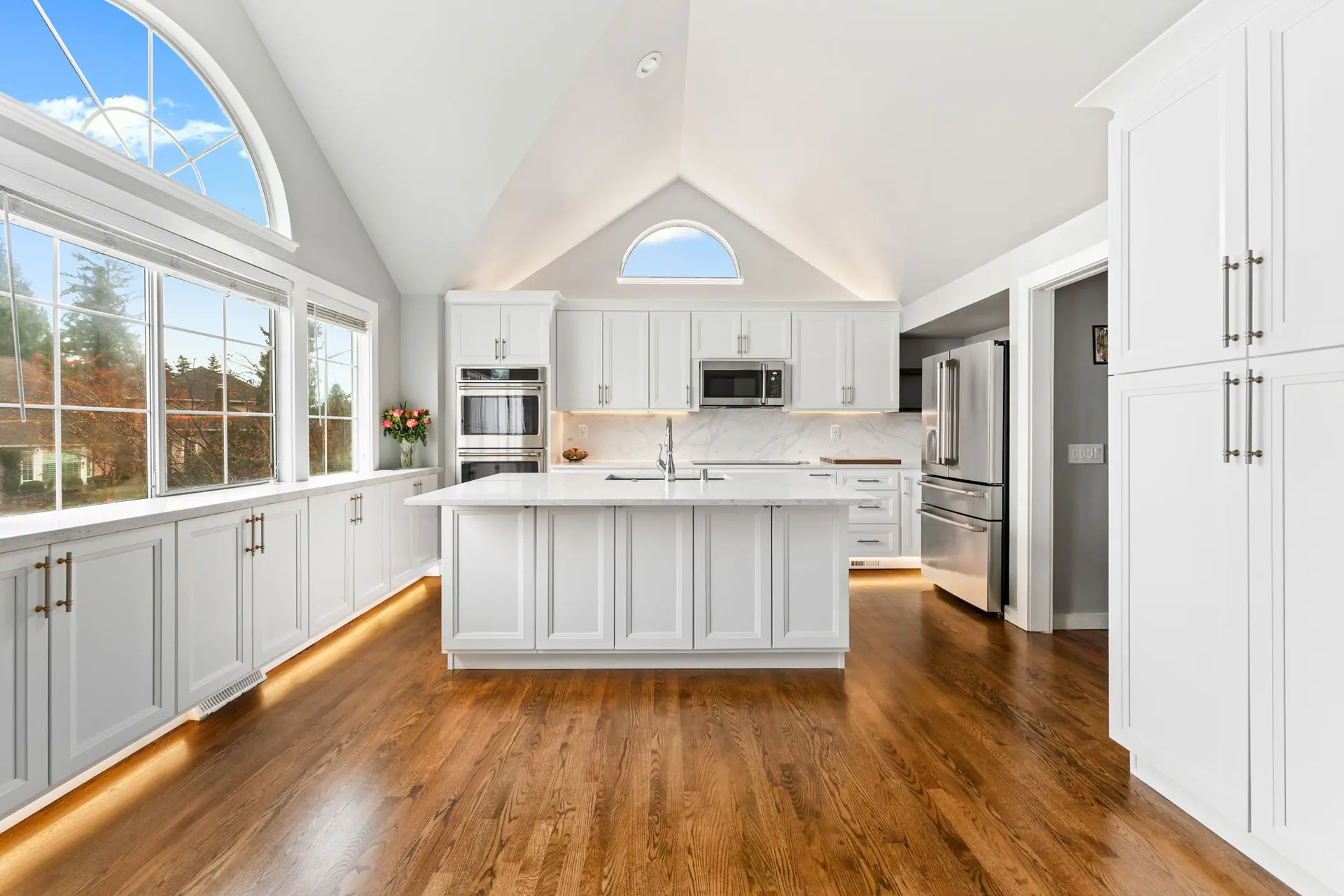 Vaulted-ceiling kitchen with white cabinets, a large island, arched windows and toe-kick lighting