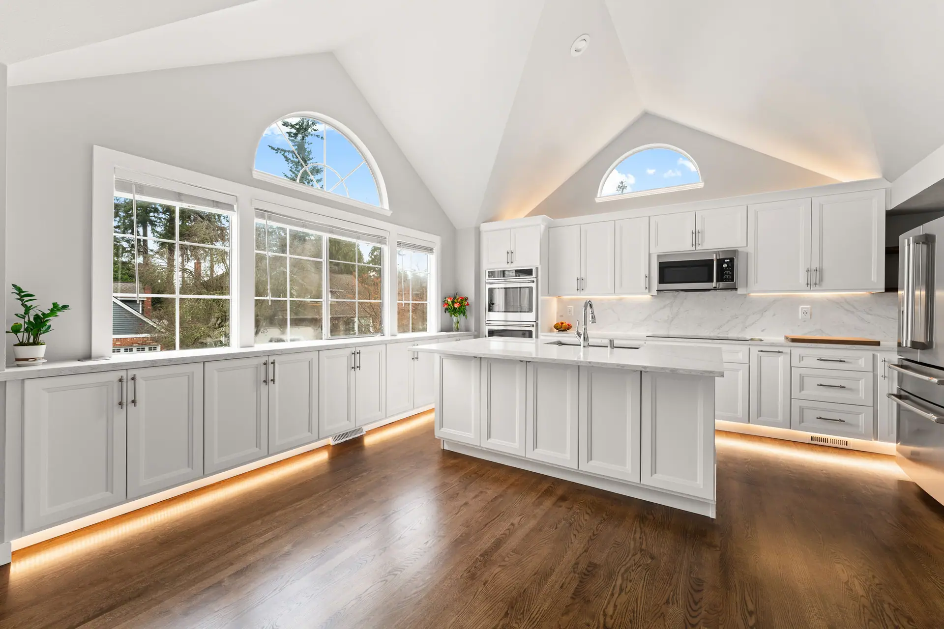 White kitchen cabinets along a wall of windows with warm toe-kick lighting