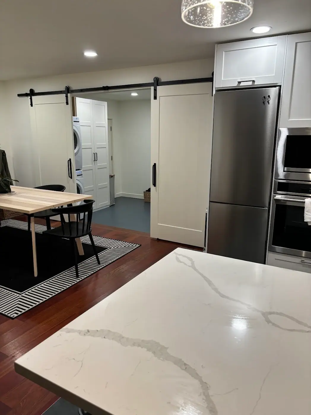 White kitchen cabinets and a stainless refrigerator beside sliding barn doors, seen across a veined countertop