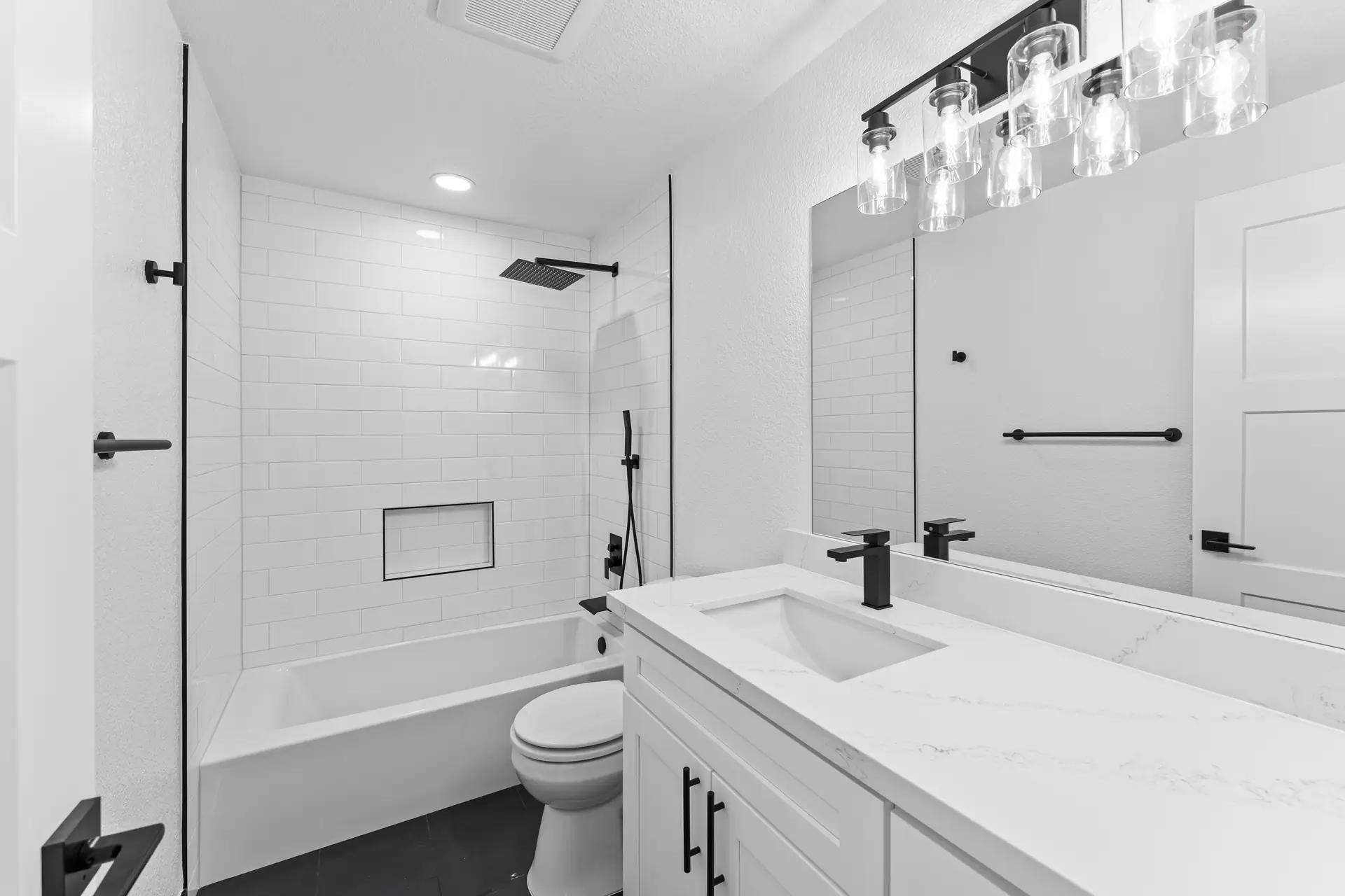 Bathroom with a white subway tile tub surround, niche, white shaker vanity, matte black fixtures and dark floor tile