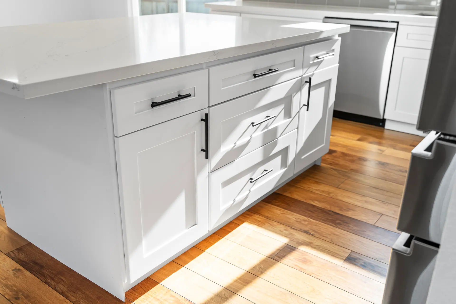 Close-up of a white shaker island with black pulls and a white countertop