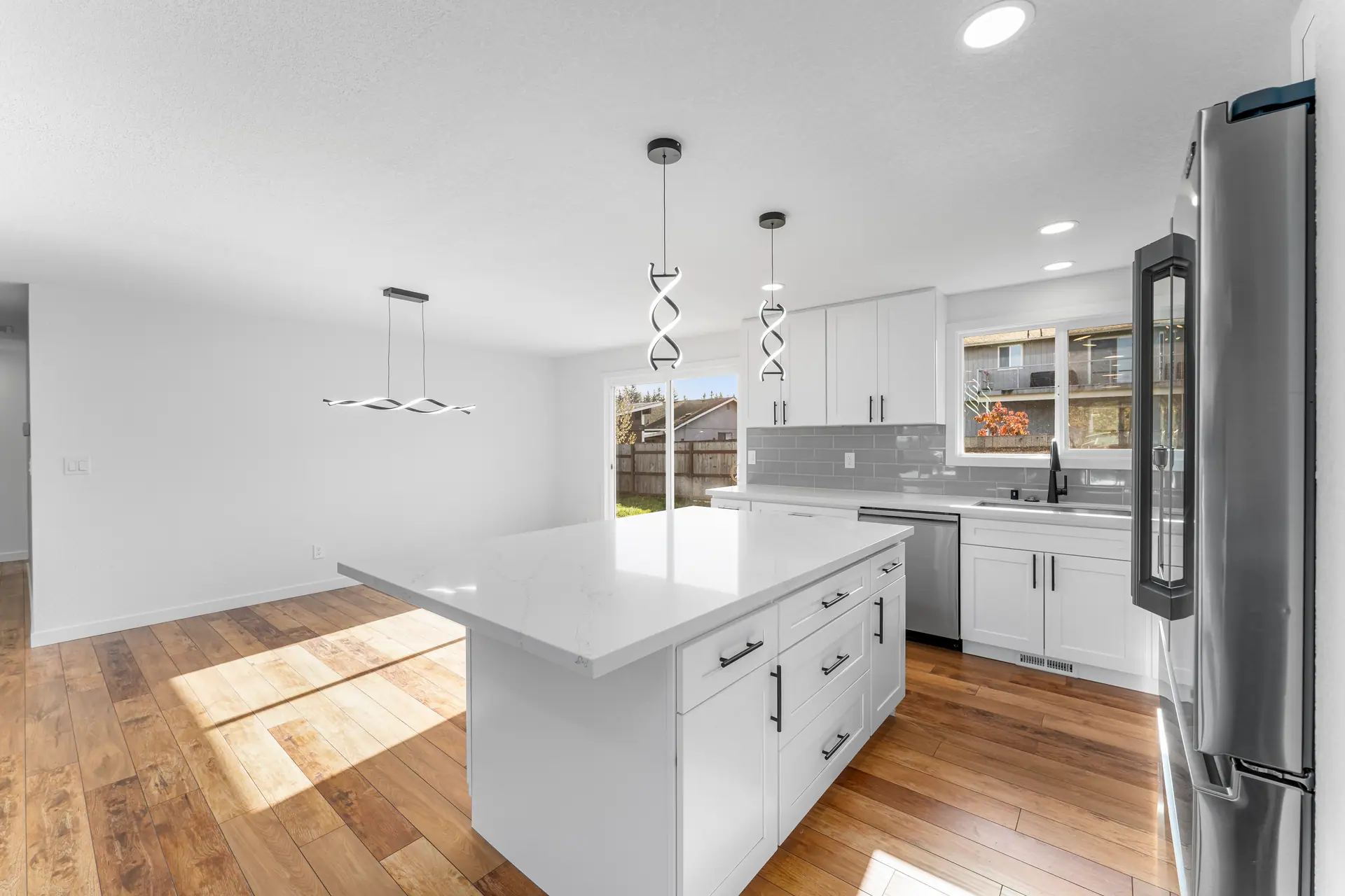 White shaker kitchen with a large island, gray subway tile backsplash, pendant lights and wood-look flooring