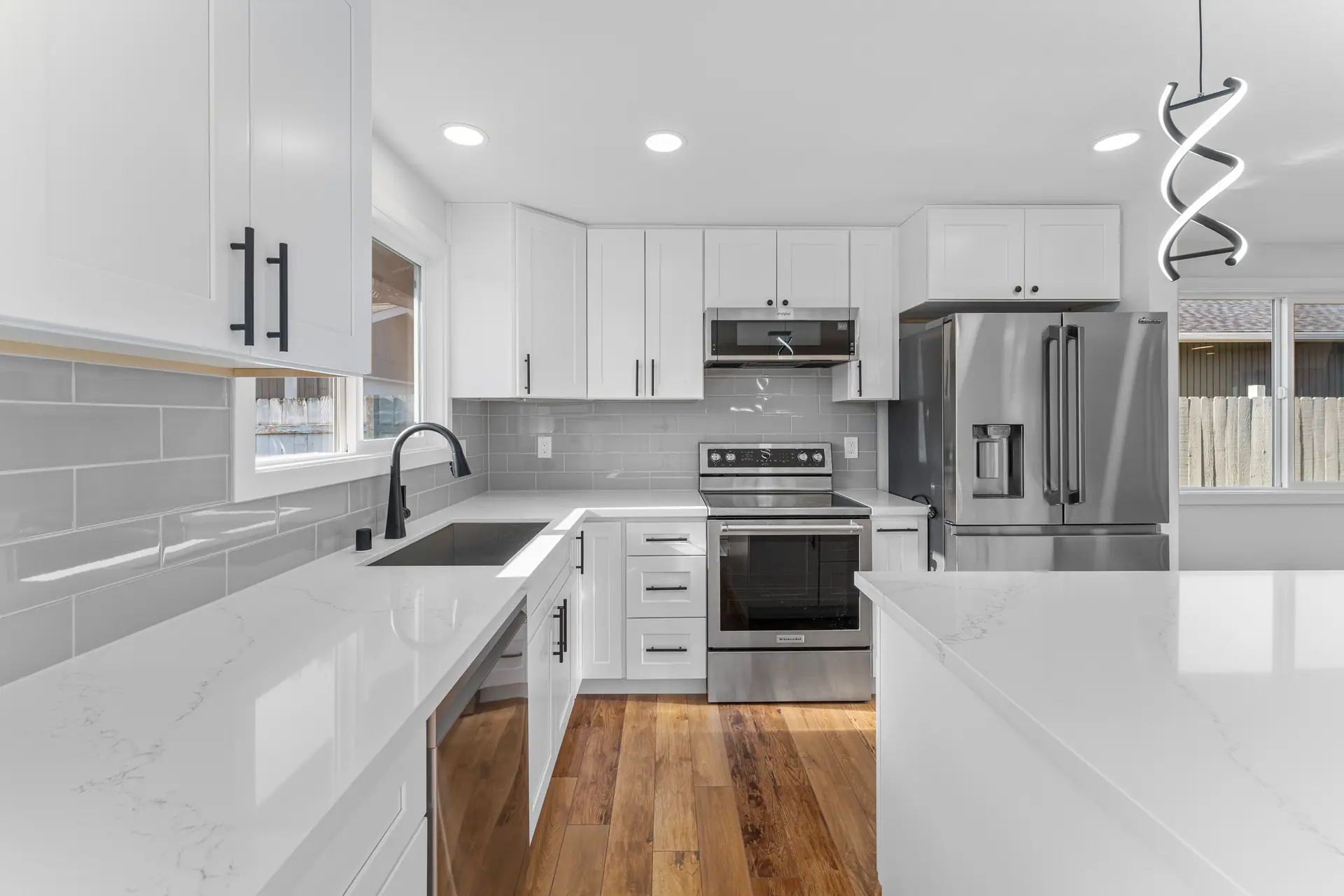 Kitchen sink run with white shaker cabinets, gray subway tile and stainless appliances