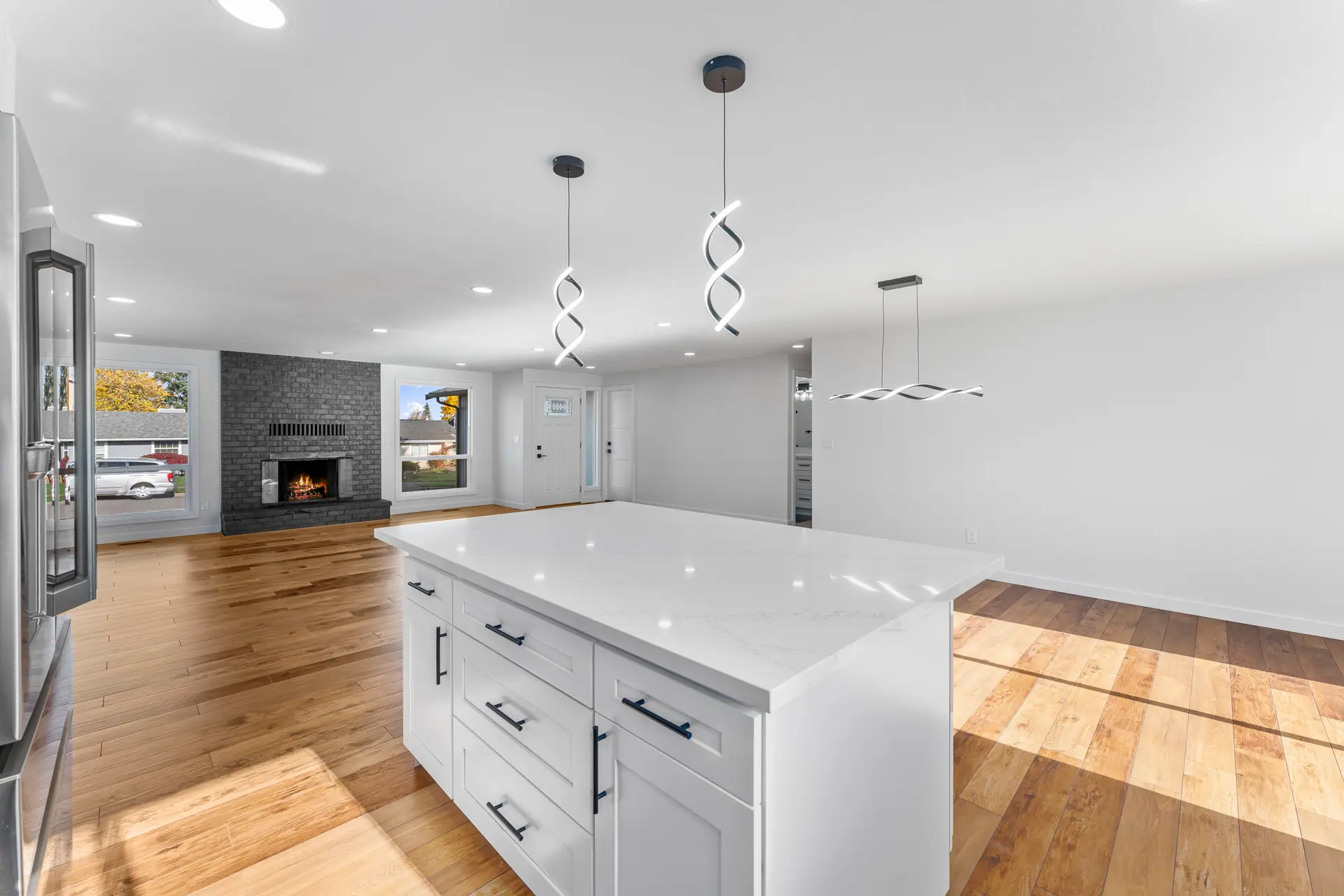 Kitchen island with pendant lights, open to a living room with a fireplace