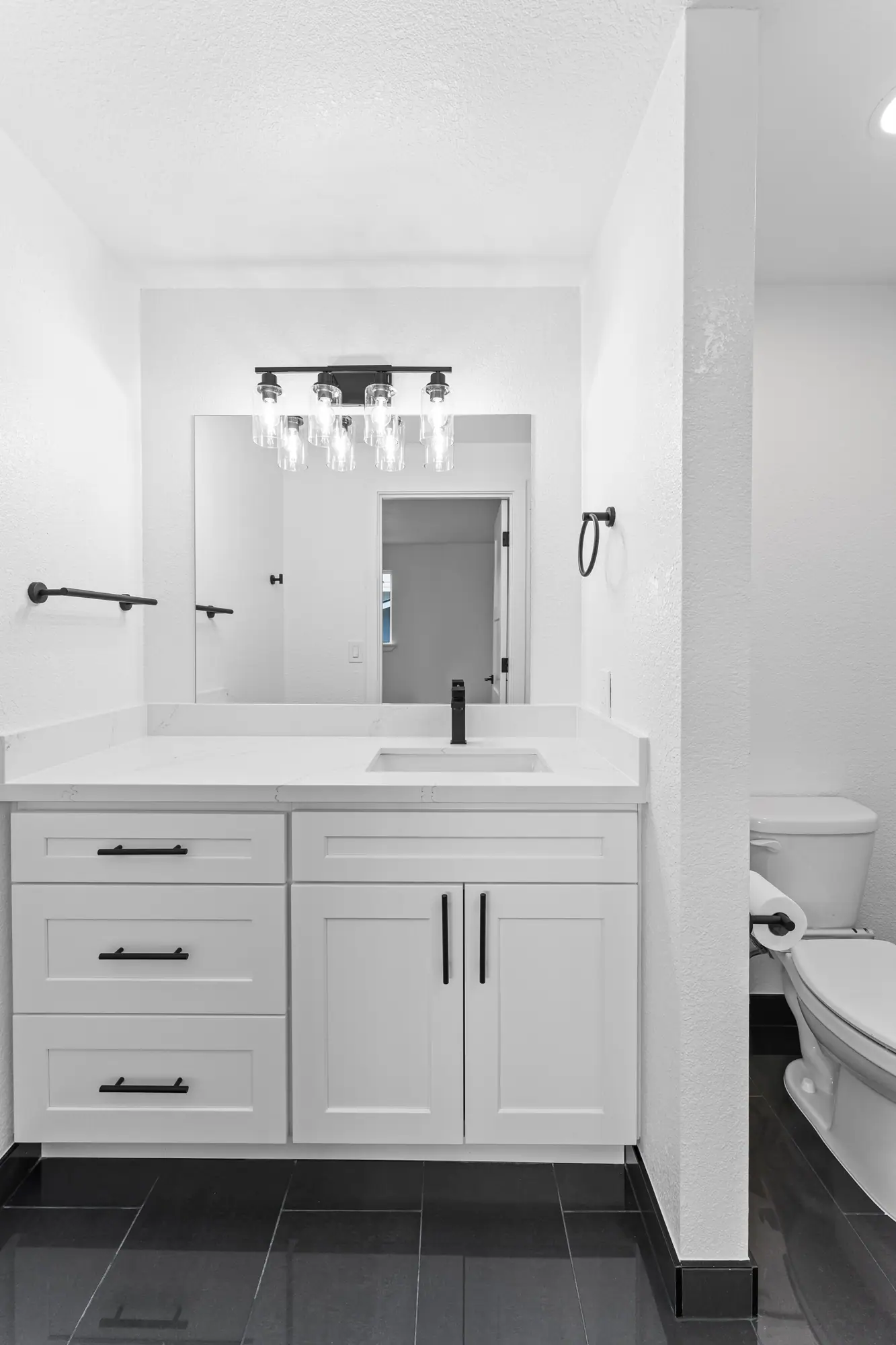 White shaker vanity with matte black hardware and a four-light fixture