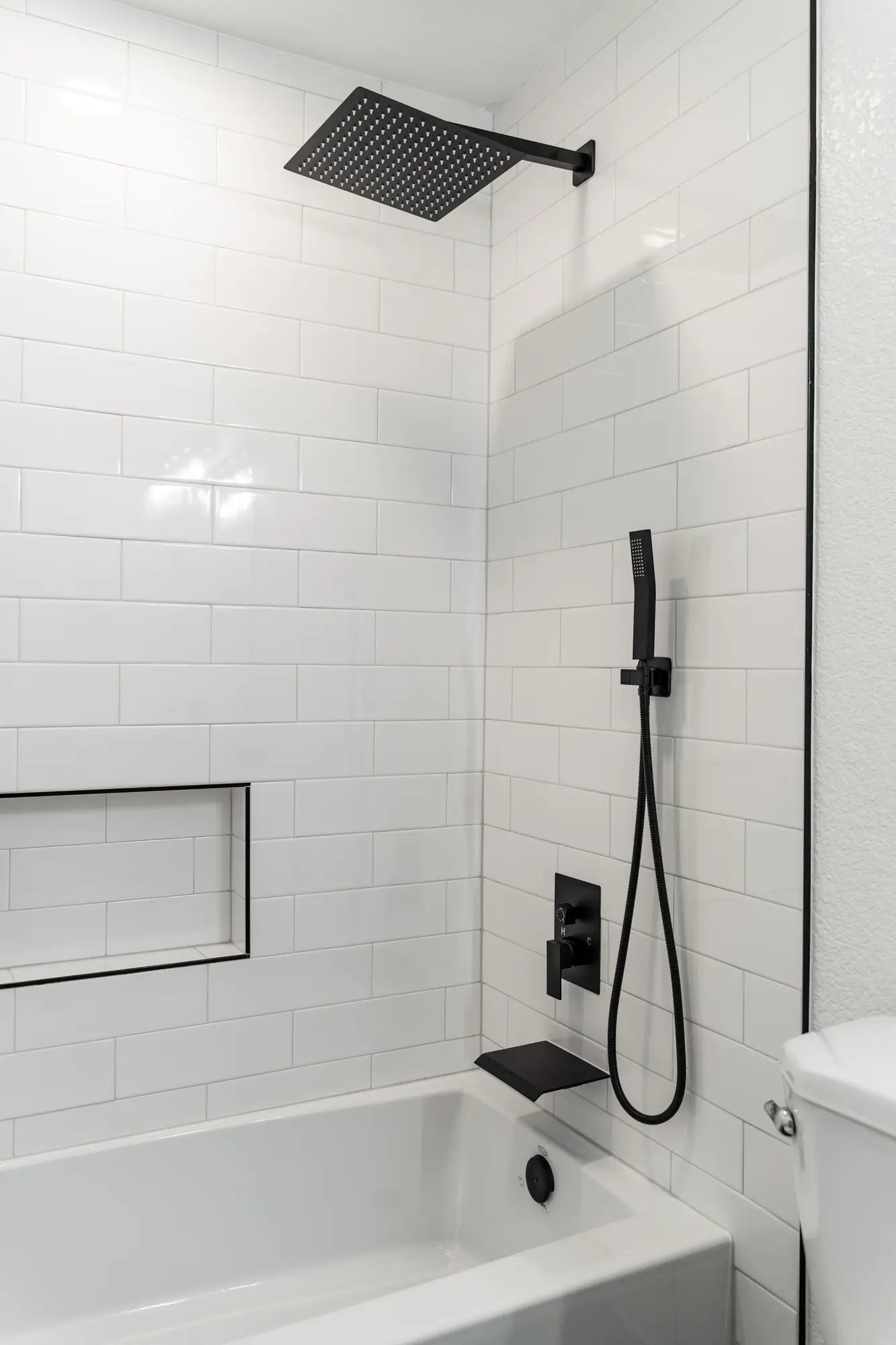 Tub and shower with white subway tile, a black-trimmed niche and a matte black rain shower