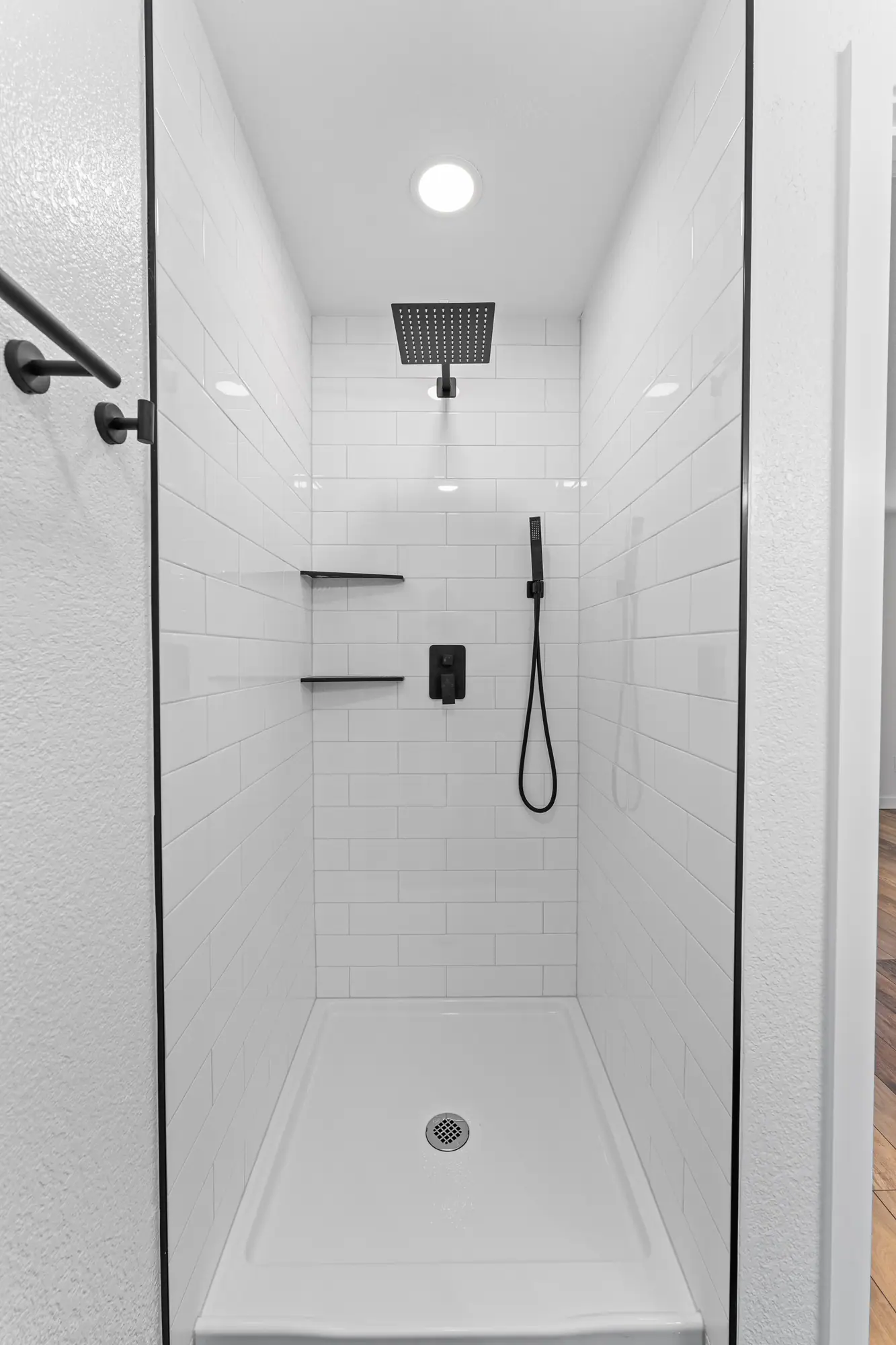 Walk-in shower with white tile, glass enclosure and matte black fixtures